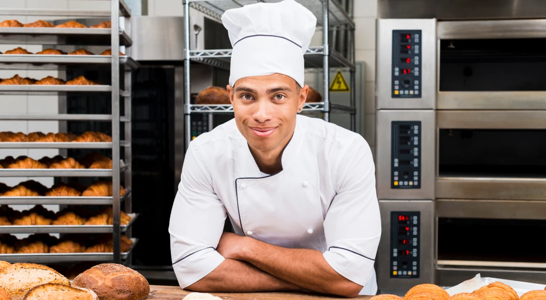 Baker in a commercial kitchen with bread and croissants